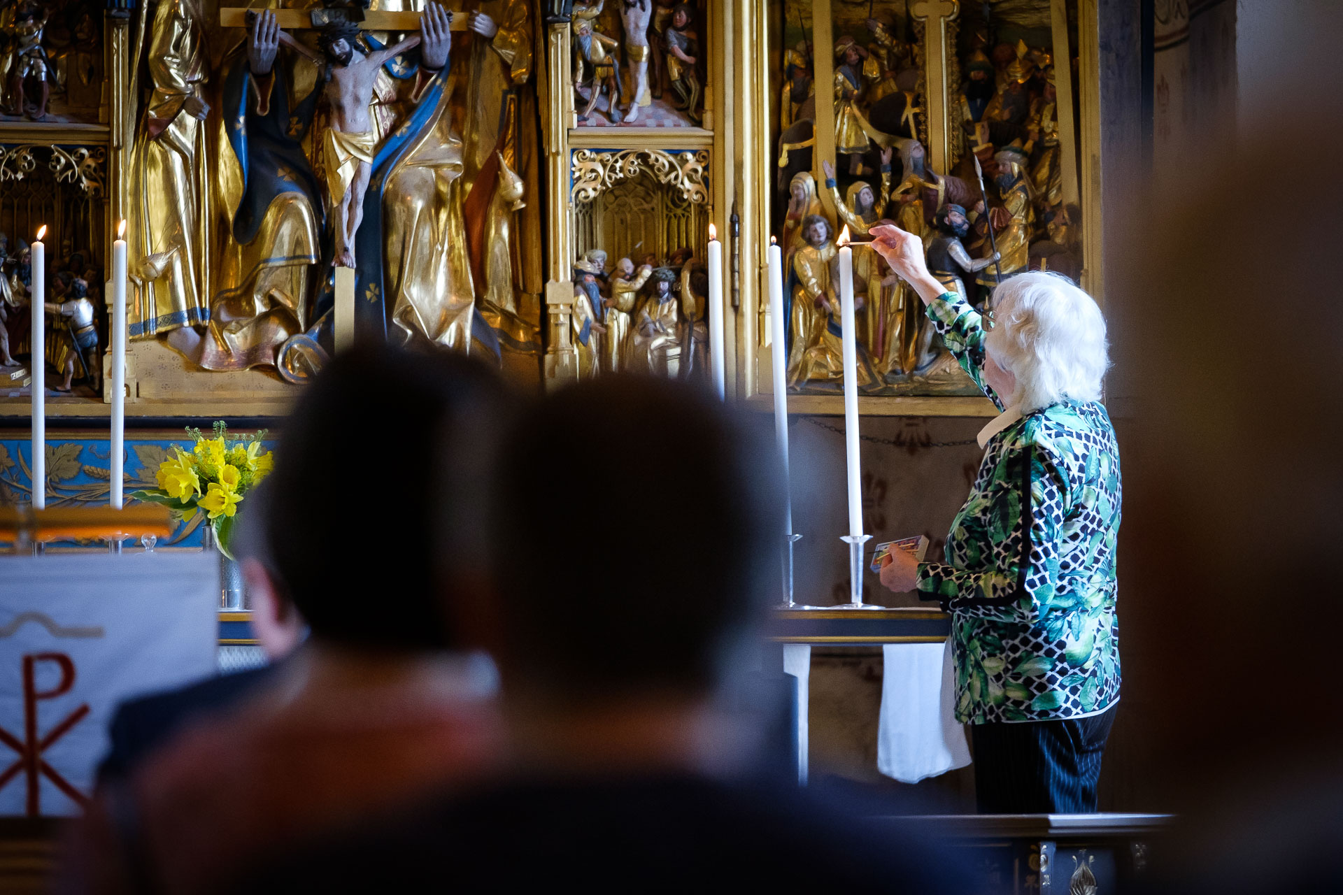 Äldre kvinna tänder höga ljus längst fram i kyrkan.