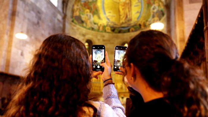 Två flickor står med ryggen mot kameran och fotograferar i ett kyrkorum med sina mobiler.