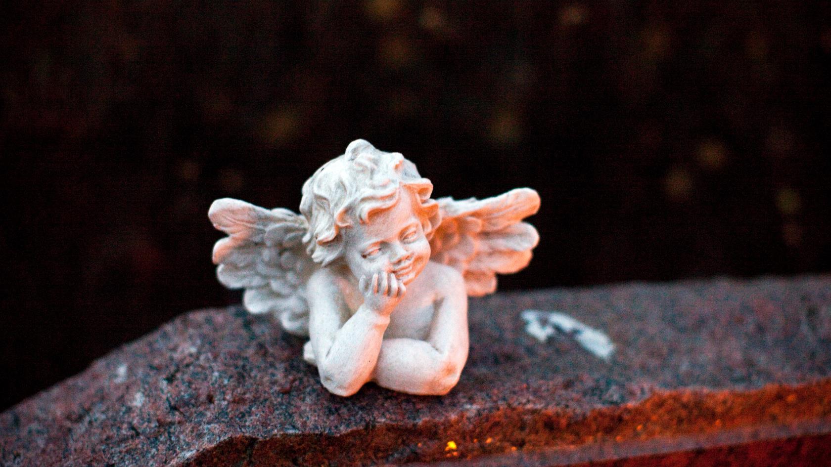 En liten vit ängel i sten ligger på en gravsten.