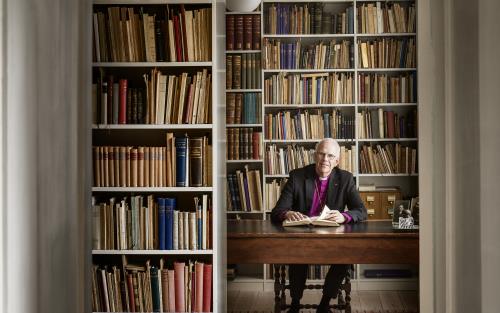 Ärkebiskop Martin Modéus sitter vid ett skrivbord i ett rum med bokhyllor.