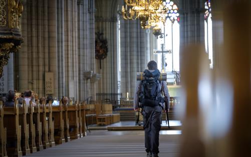 En man med stor ryggsäck går mellan kyrkbänkarna i Uppsala domkyrka.