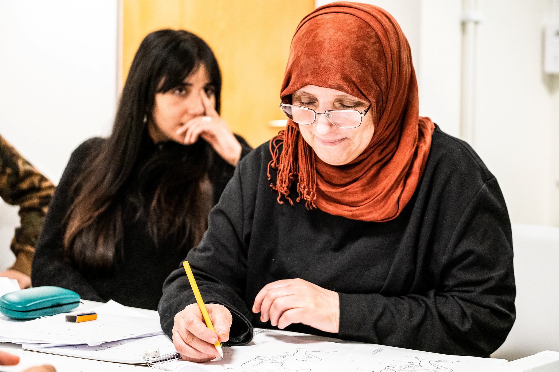 Två kvinnor som deltar på språkundervisningen sitter vid ett bord och skriver.