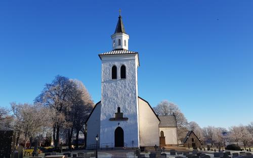 Åby kyrkas torn mot en blå himmel med frostiga träd runt omkring