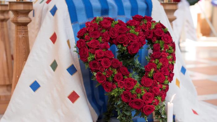 En begravningskrans i form av ett stort hjärta med rosor vilar mot en kista.