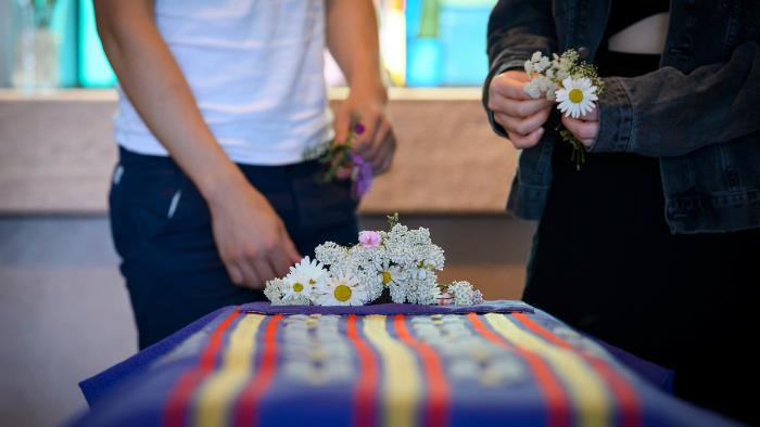 Ett par personer lägger blommor på kistan vid en begravning
