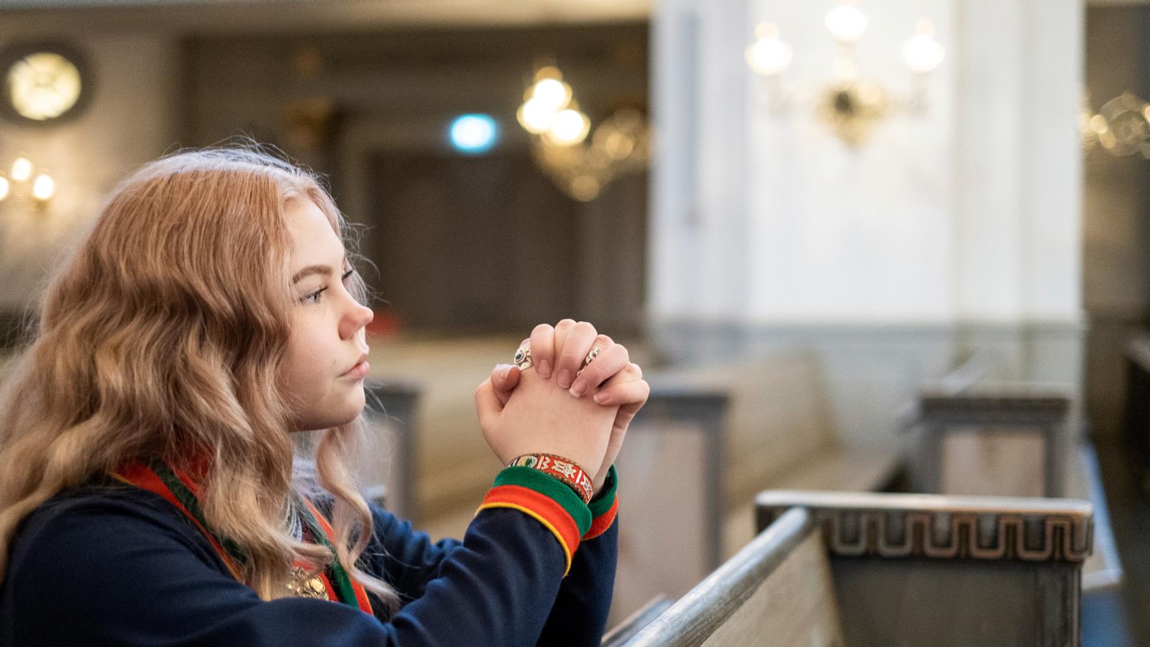 Flicka ber i kyrka och bär traditionella samekläder