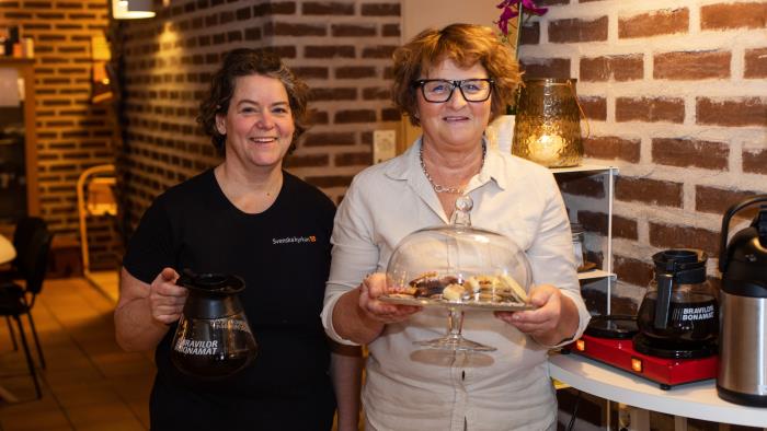 Två kvinnor som håller fram fika. En kvinna med en kaffekanna och en kvinna med ett kakfat.