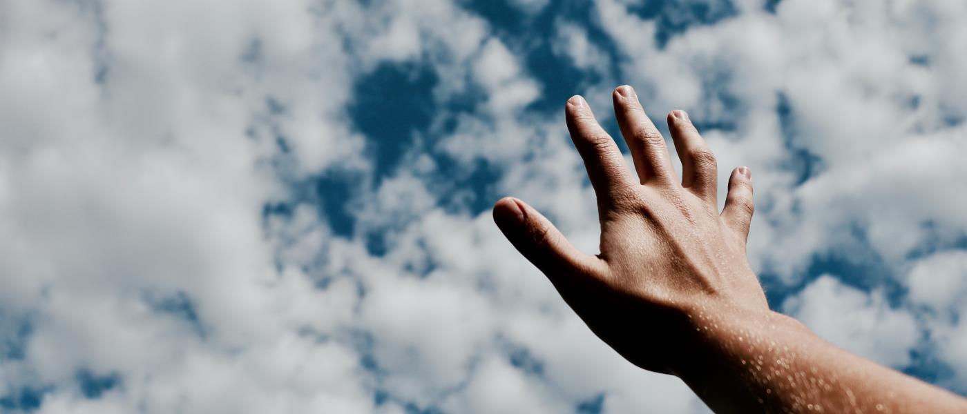 Hand som sträcker sig mot molnig himmel. 