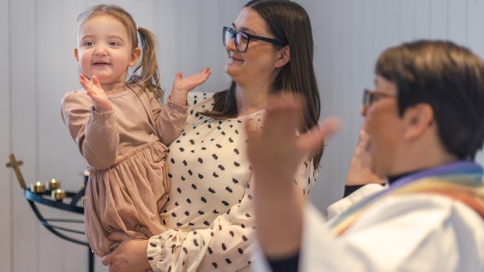 Mamma, barn och präst ler och skrattar under dop i Svenska kyrkan