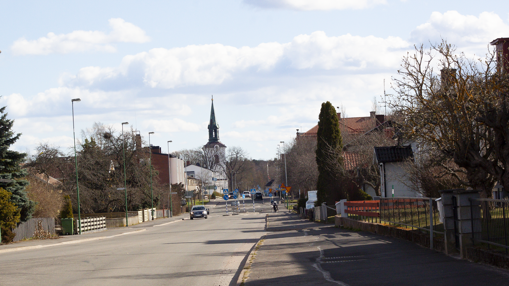 vy över Tidaholm med TIdaholms kyrka i centrum, bilar kör på vägen som omges av hus på vardera sida.