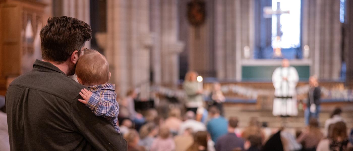 Barnmässa i Uppsala domkyrka. En pappa håller sitt lilla barn i famnen medan de blickar mot prästen som står vid altaret.