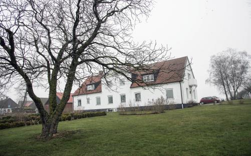 Bilden föreställer ett stort vitt hus med rött tegeltak.