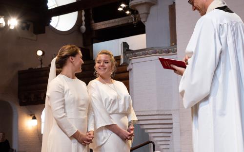 En vigsel mellan två kvinnor i brudklänningar i Masthuggskyrkan. Brudparet står framför prästen.