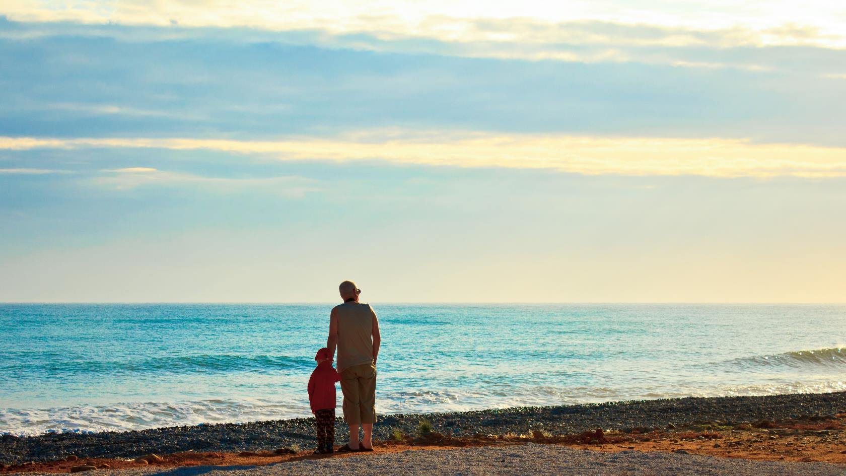 En vuxen och ett barn står vid strandkanten och tittar ut över vattnet.