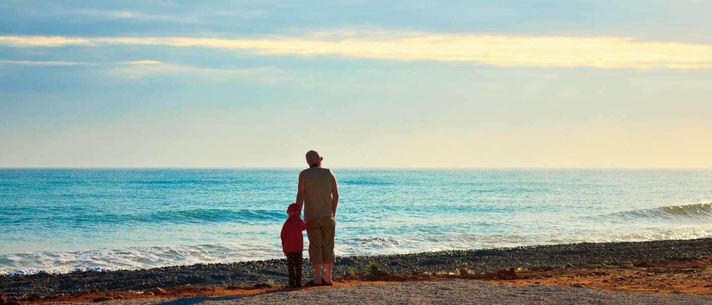 En vuxen och ett barn står vid strandkanten och tittar ut över vattnet.