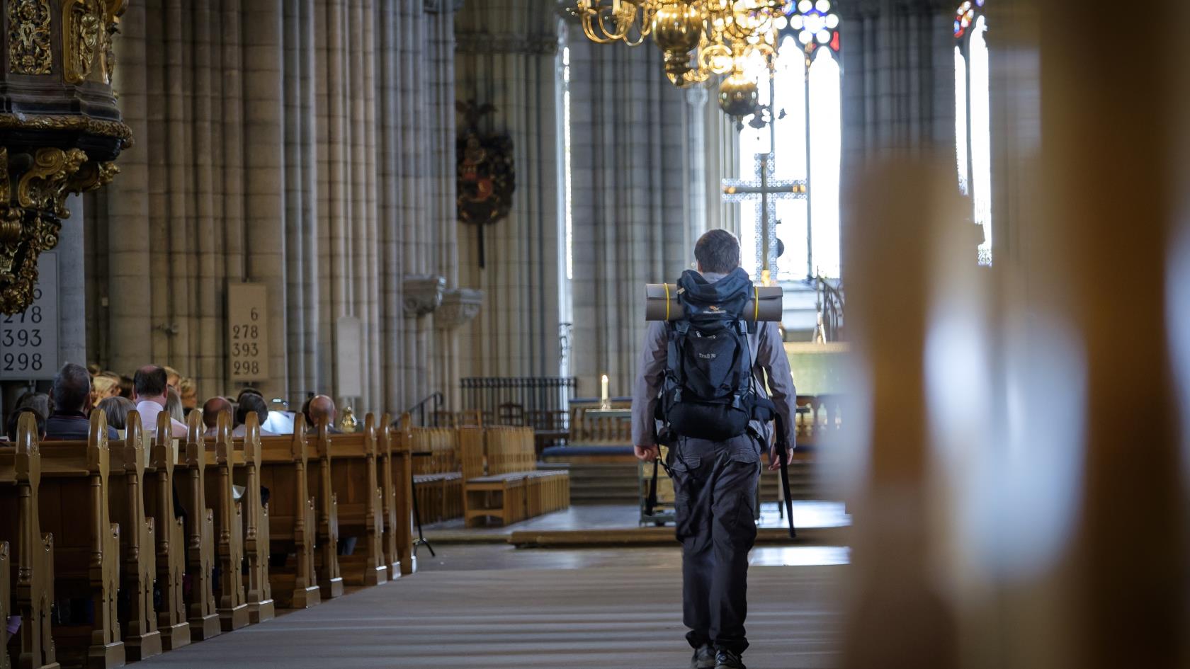 En man med stor ryggsäck går mellan kyrkbänkarna i Uppsala domkyrka.
