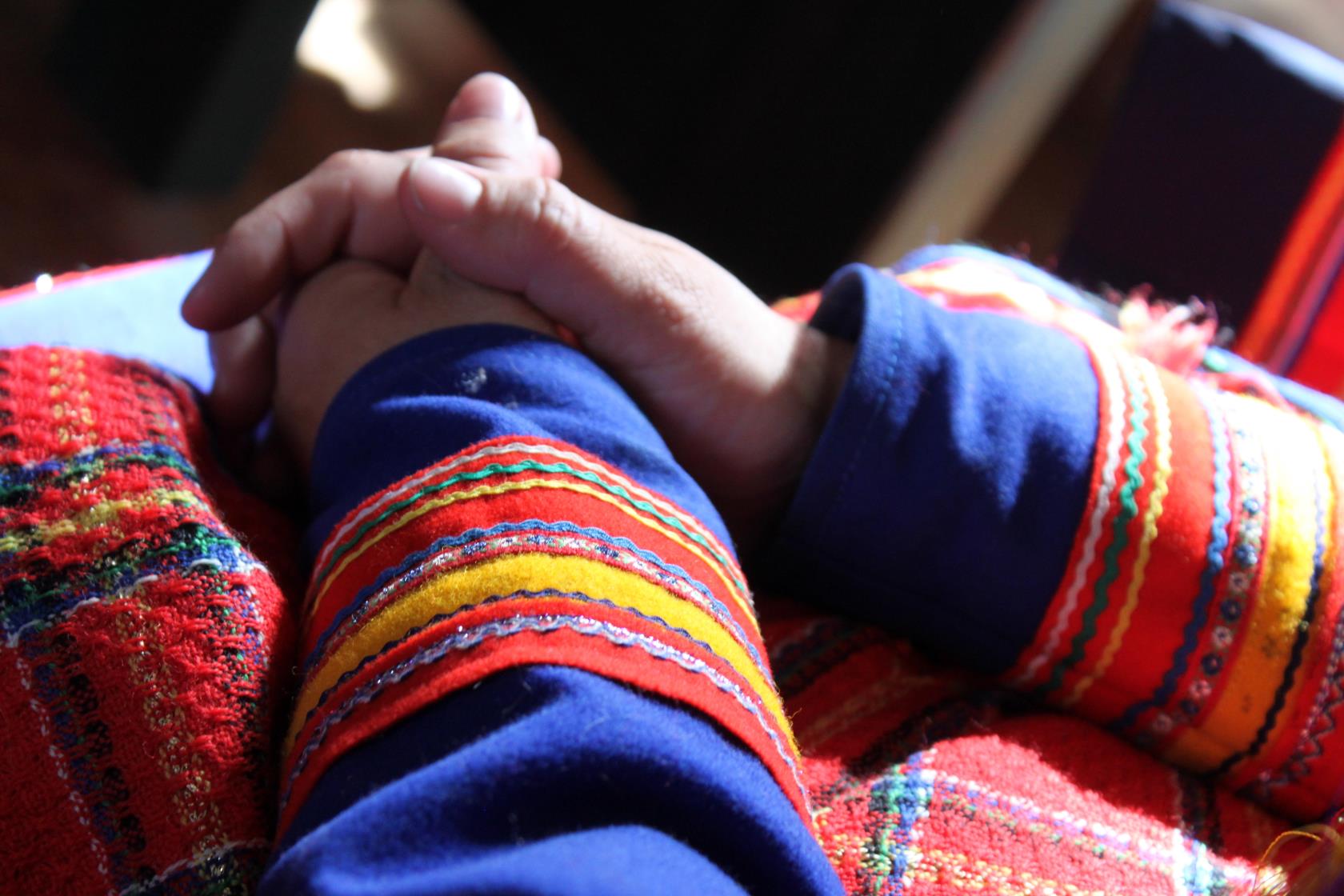 En person i samiska kläder sitter med knäppta händer.