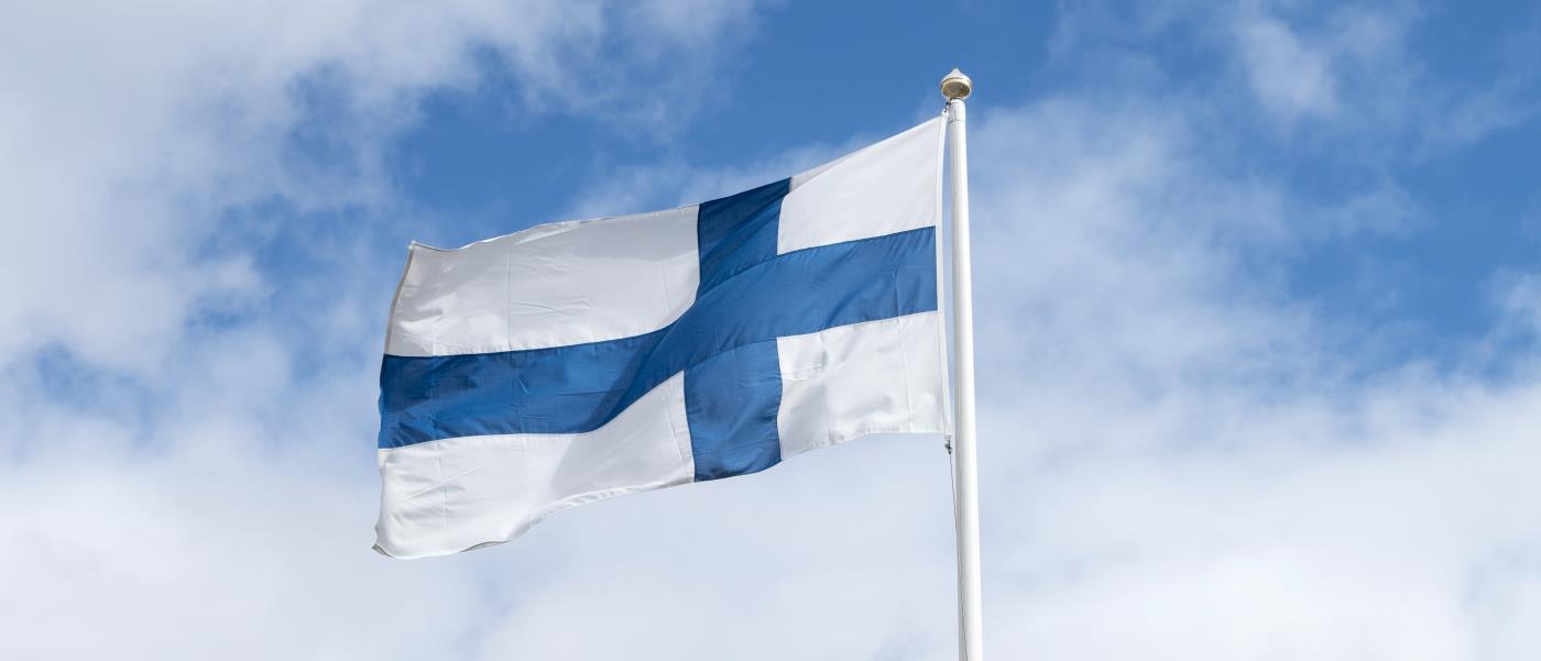 En flaggstång med finska flaggan mot en blå och molnig himmel.