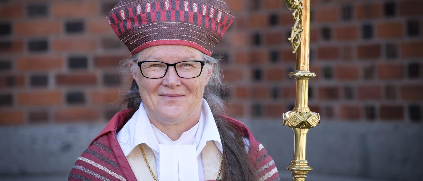 Porträttbild på biskop Åsa Nyström i röd ämbetsdräkt och kräkla i handen.