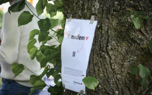Ett papper med texten Bli medlem och en pil till en QR-kod sitter fasttejpat på ett träd.