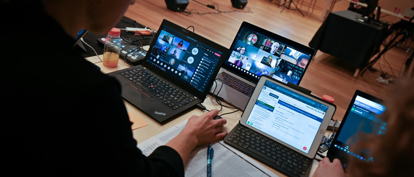 Några personer arbetar framför flera uppställda laptop-datorer.