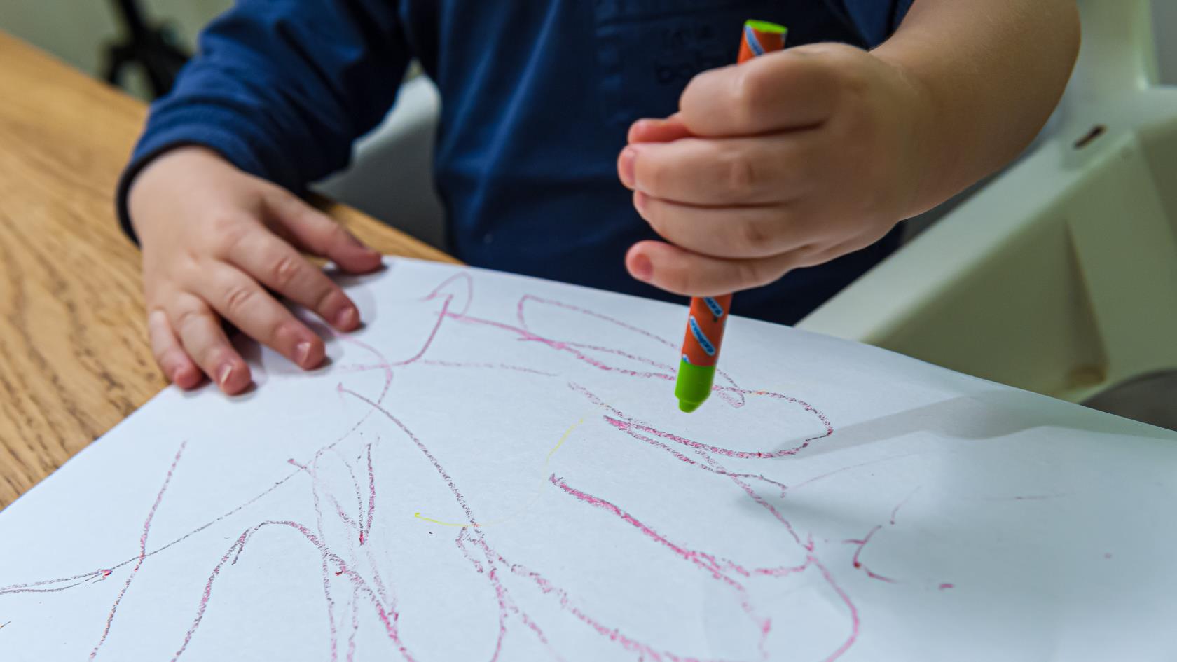 Ett barn ritar med kritor på ett papper.