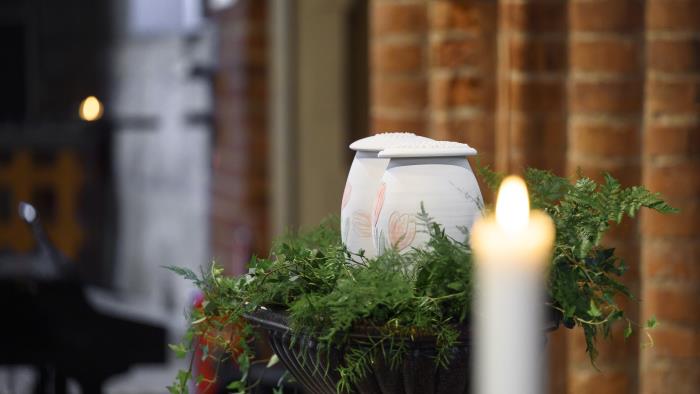 Två urnor med handmålade tulpaner står bland ormbunksblad på ett bord i kyrkan. Ett tänt ljus i förgrunden.