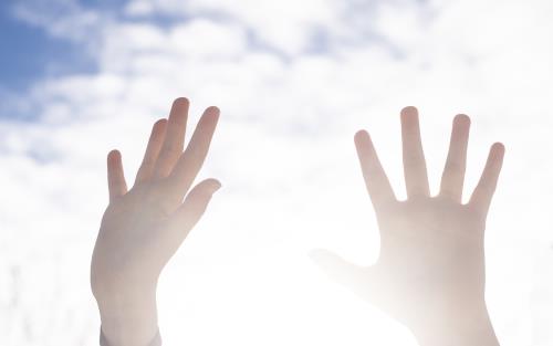 Närbild på två händer som sträcks upp mot himlen.