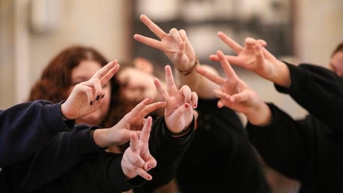 En grupp ungdomar i svarta tjocktröjor gör freds-tecken med händerna.