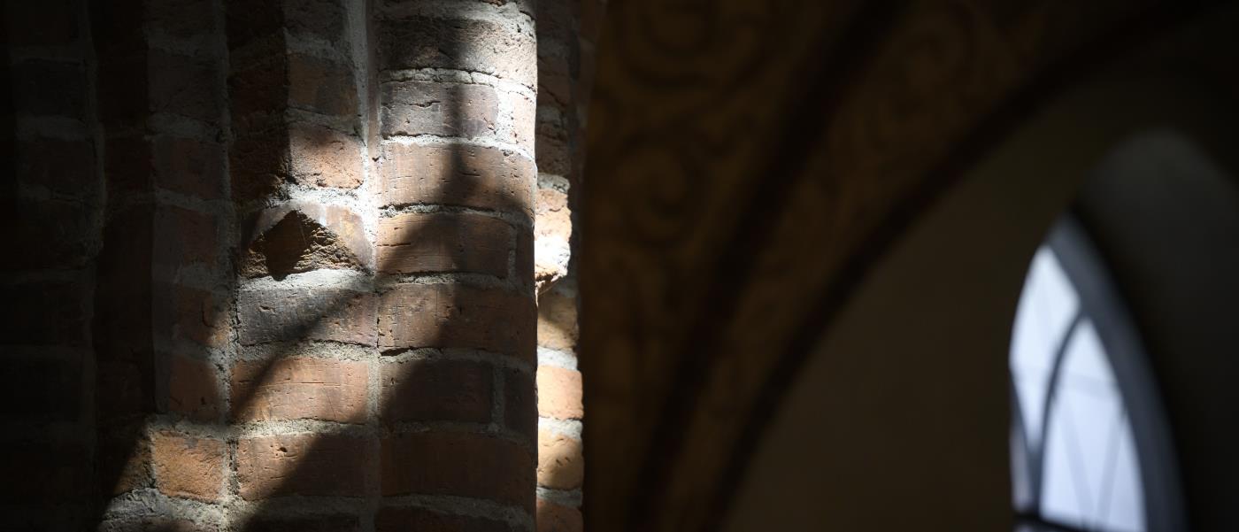 Solljuset skiner in på några pelare i rött tegel i en kyrka.