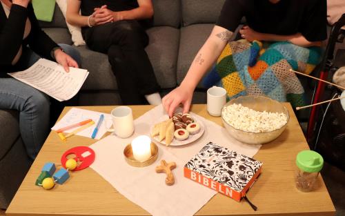 Personer sitter runt ett bord med ljus, bibel, popcorn, fika, leksak, garnnystan med mera.