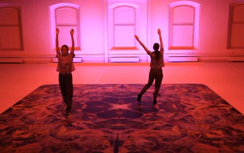 Två kvinnor dansar med händerna uppsträckta i ett stort rum.