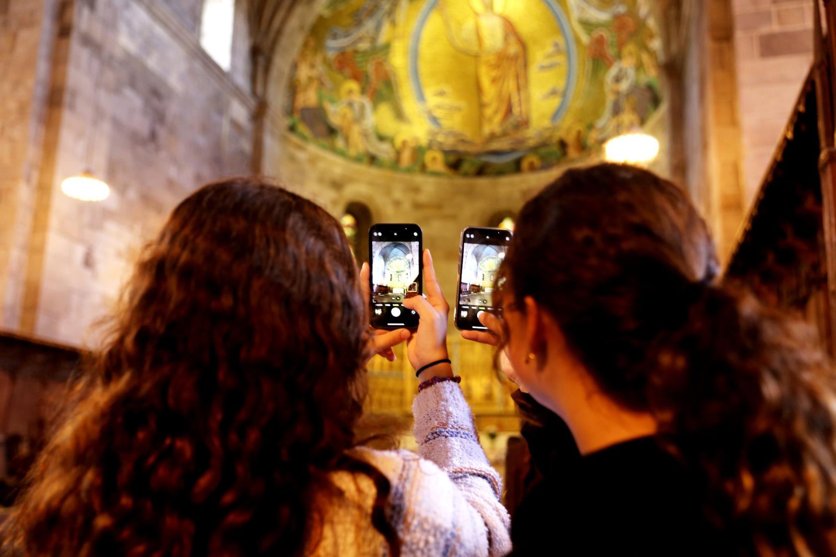 Två flickor står med ryggen mot kameran och fotograferar i ett kyrkorum med sina mobiler.
