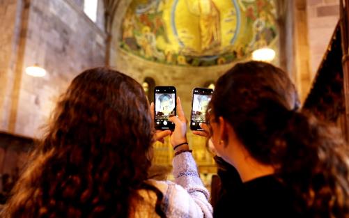 Två flickor står med ryggen mot kameran och fotograferar i ett kyrkorum med sina mobiler.