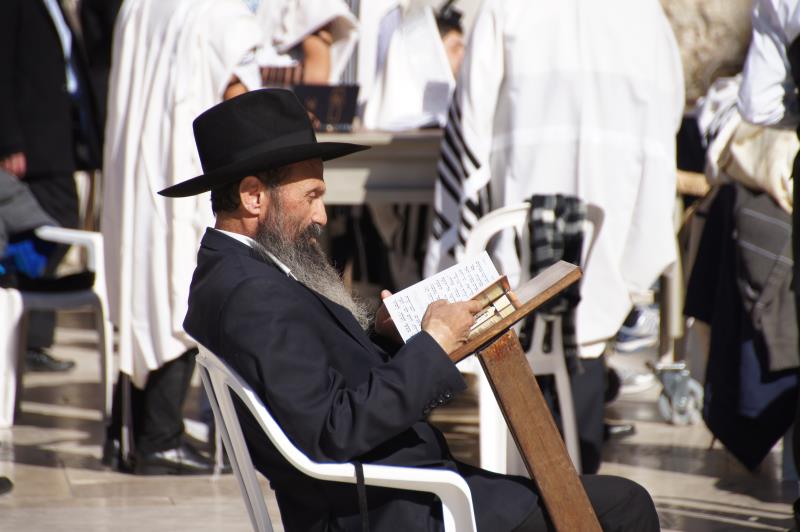 Judisk man med hatt sitter ute och läser Bibeln.