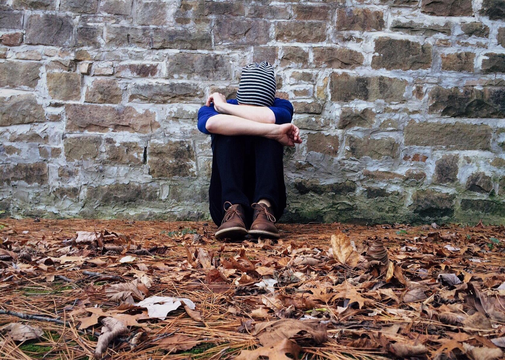 Person sitter ensam vid en vägg och gömmer ansiktet i armarna.