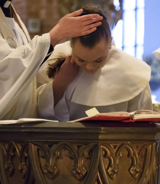 En ung tjej i vit konfirmationsdräkt blir döpt.