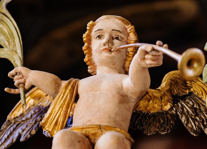 Närbild på en träskulptur som föreställer en ängel som spelar trumpet.