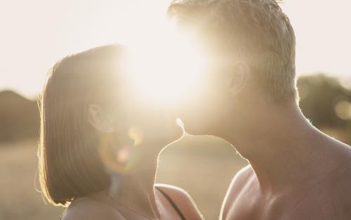 En man och en kvinna kysser varandra. Solen lyser igenom mellan deras ansikten.