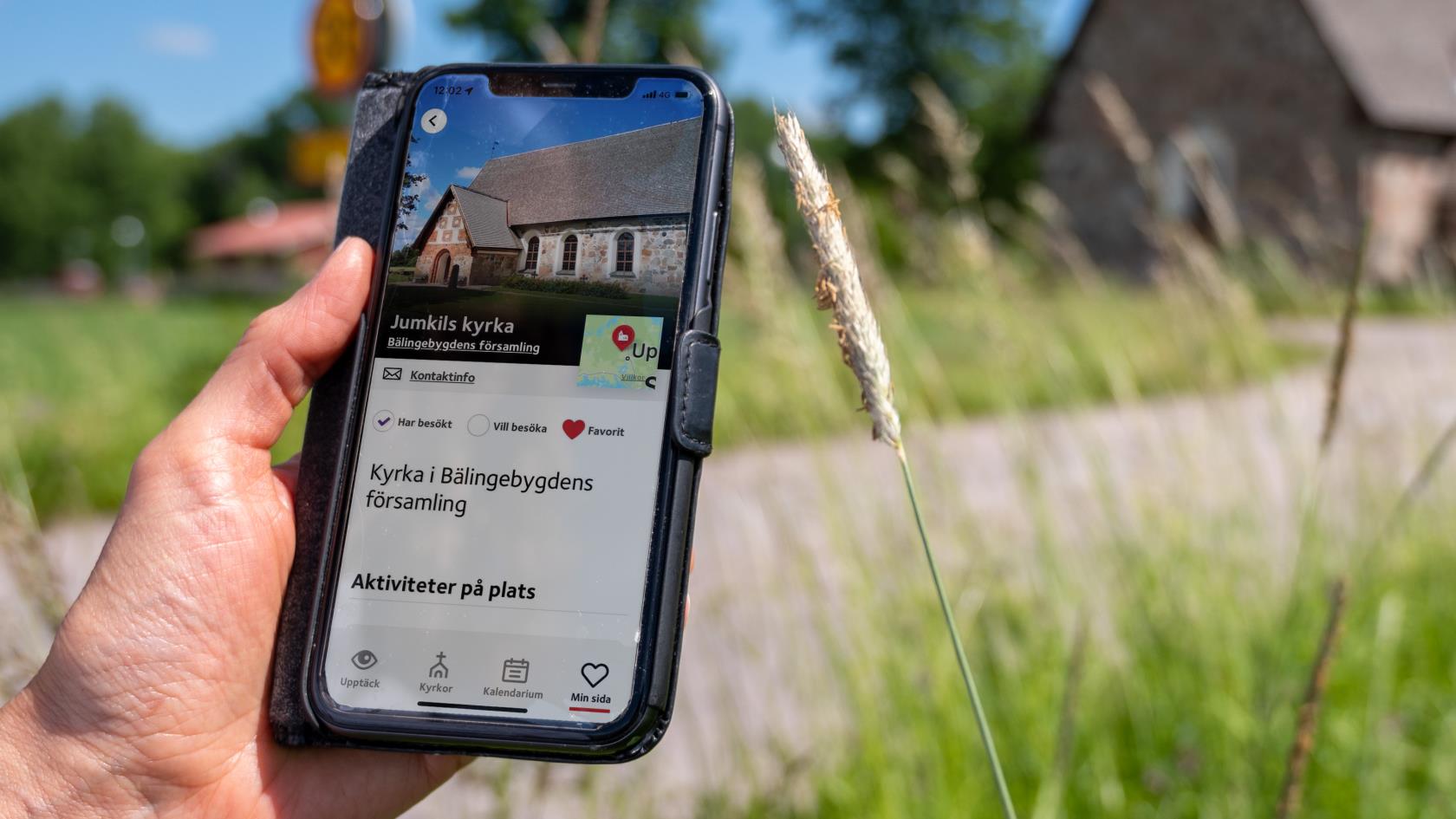 En hand håller i en mobil med skärmbild om kyrkguiden som visar adressen för kyrkan.