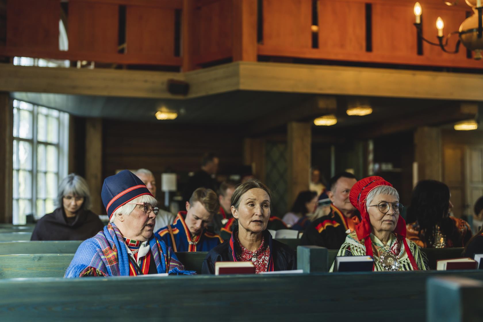 Kyrkobesökare i samiska dräkter sitter i kyrkbänkarna.