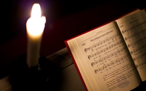 Ett stearinljus lyser i mörkret bredvid en öppen psalmbok.