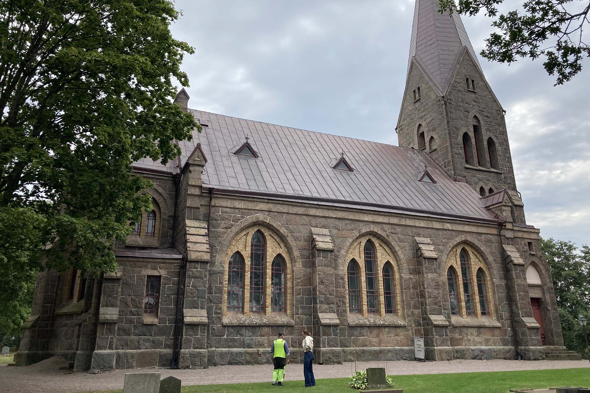 Två personer står framför en kyrka i murad natursten.