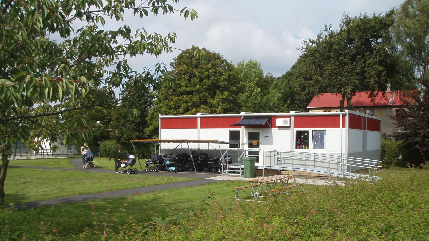 Föräldrar med barnvagnar på väg mot paviljongen bredvid församlingsgården.