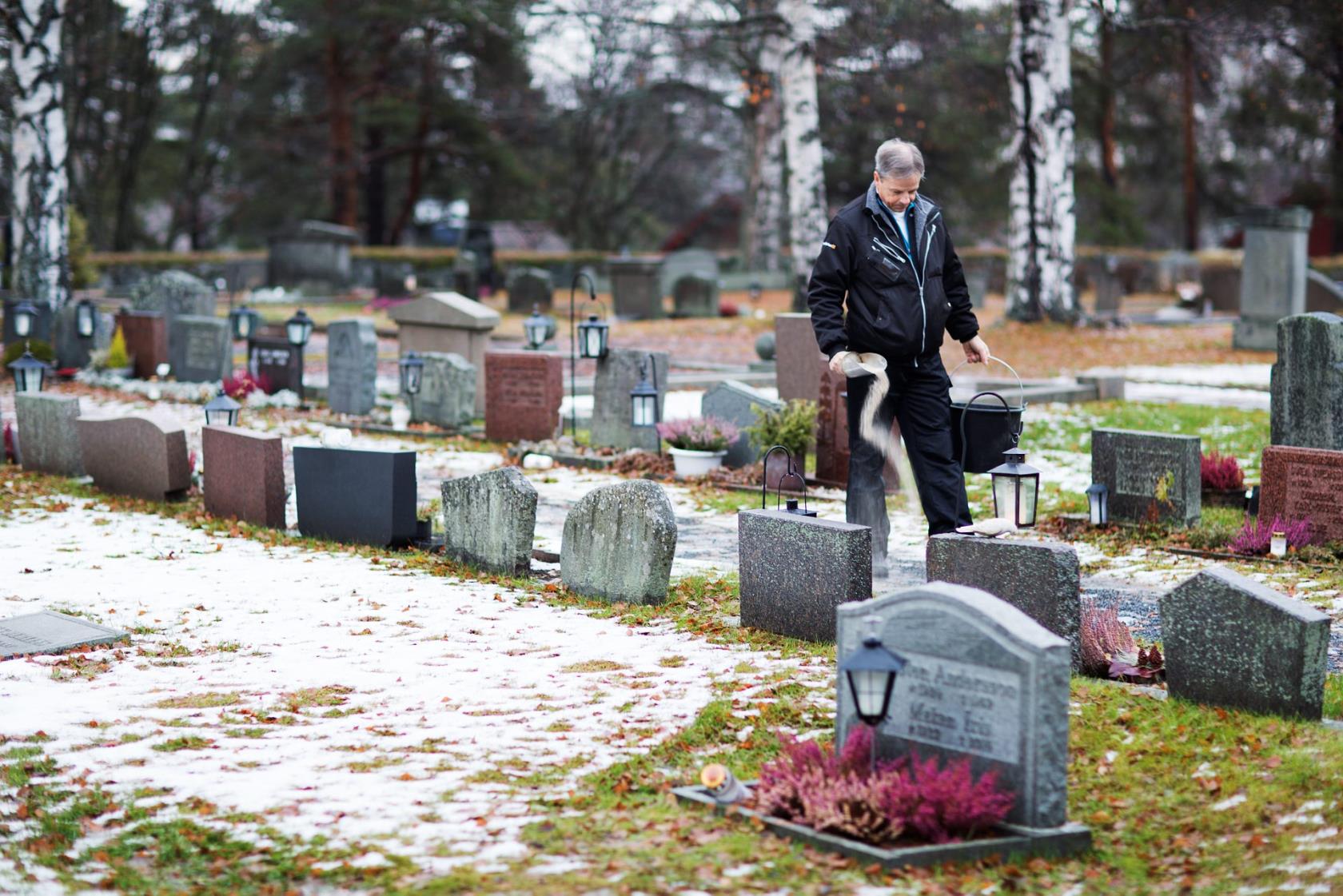 Vaktmästare sandar gångar på kyrkogården