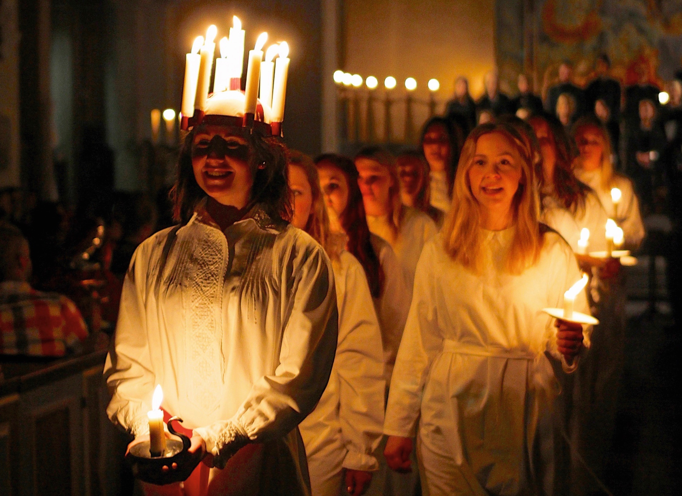 Luciatåg med lucia och och tärnor klädda i vitt med levande ljus. 