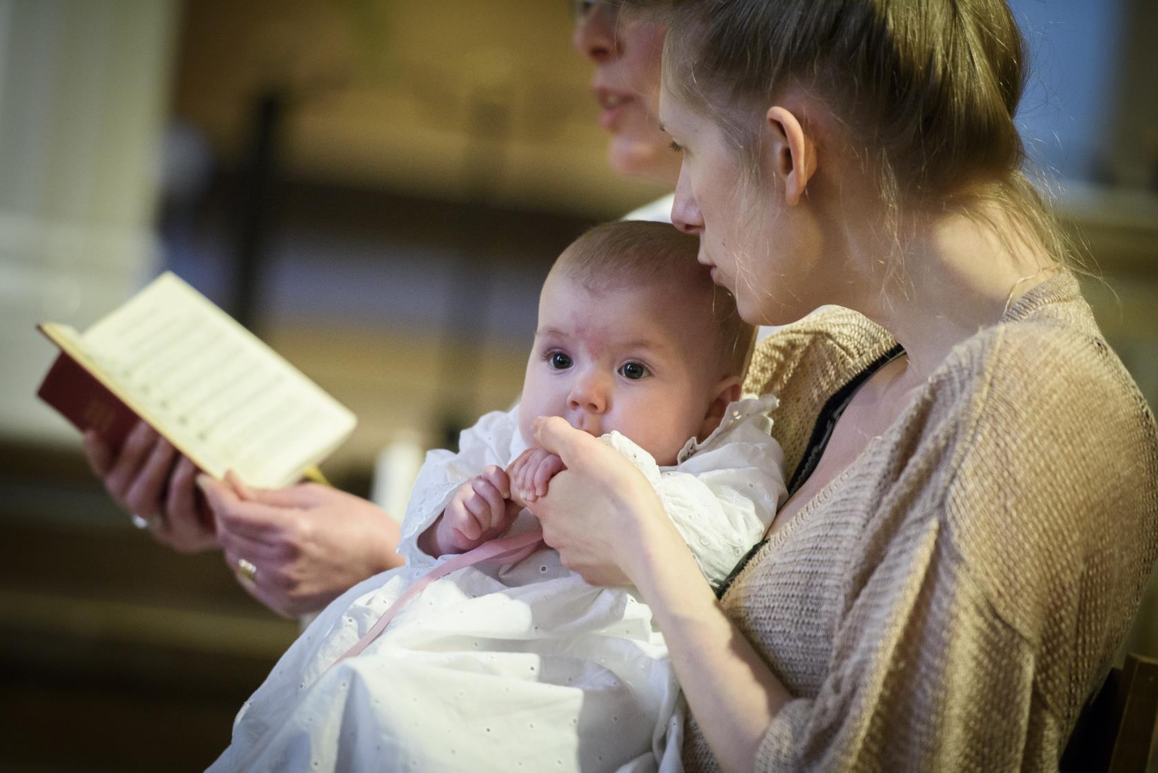 Mamma håller bebis under ett dop.