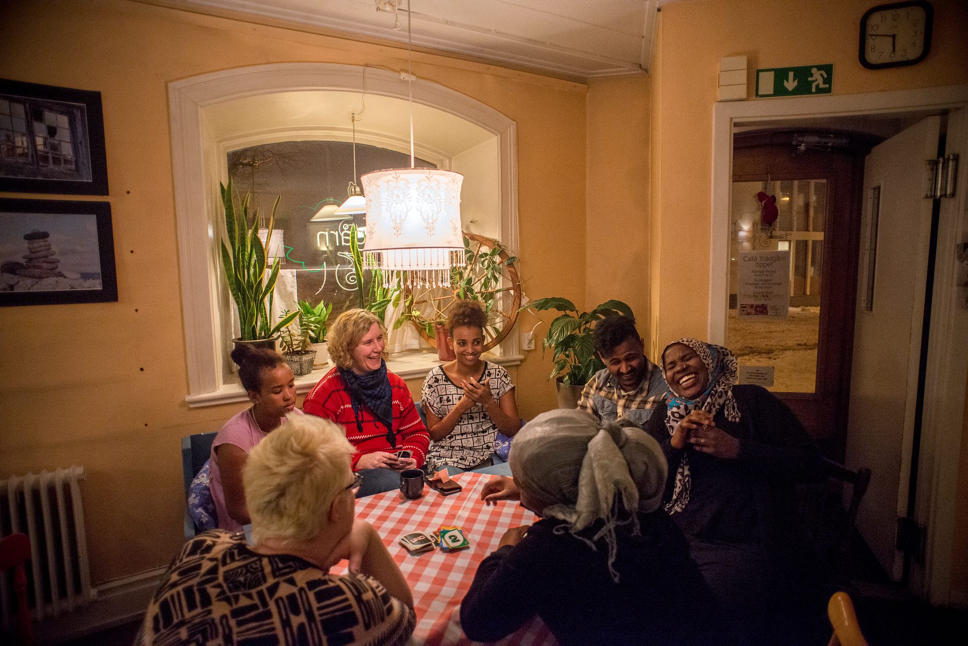 Ett brokigt sällskap av olika nationalitet och ursprung spelar sällskapsspel och skrattar kring ett bord med rutig duk.