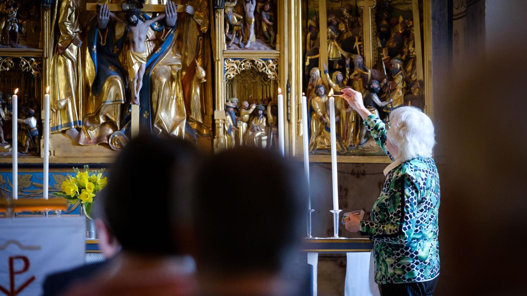 Äldre kvinna tänder höga ljus längst fram i kyrkan.