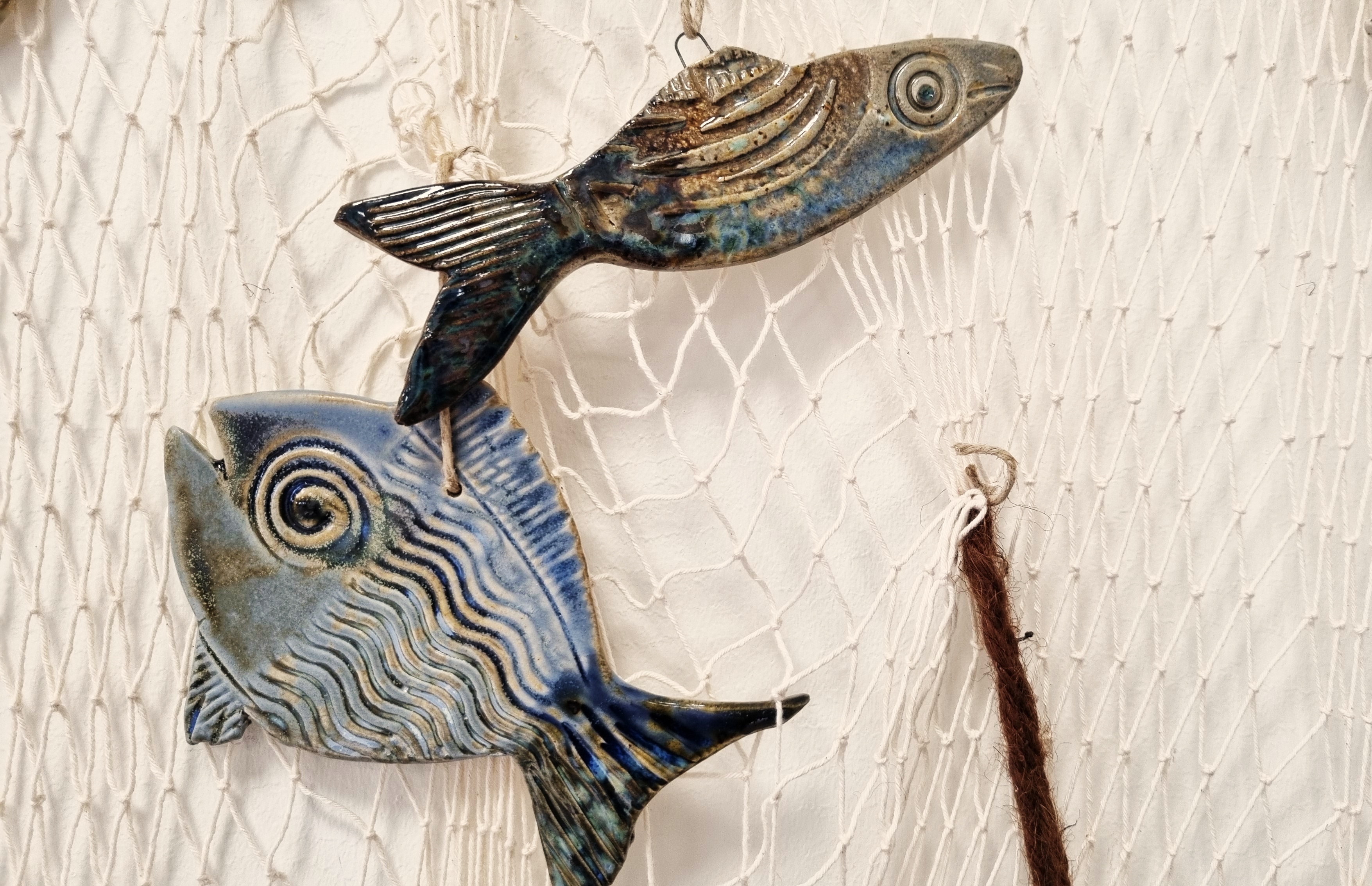 två fiskar i keramik som hänger i ett nät. 